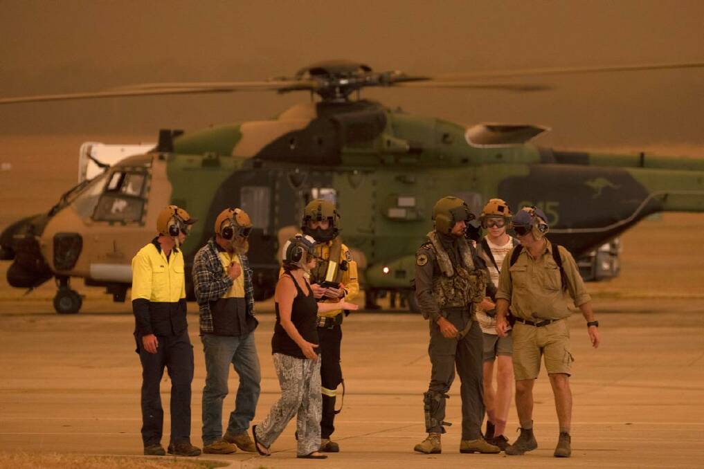 Members of the Tytherleign family are escorted from an MRH-90 at HMAS Albatross by Leading Seaman Aircrewman Ben Nixon and Rural Fire Service employee Dwyane Graham after being evacuated from their property near Tianjara in NSW.
