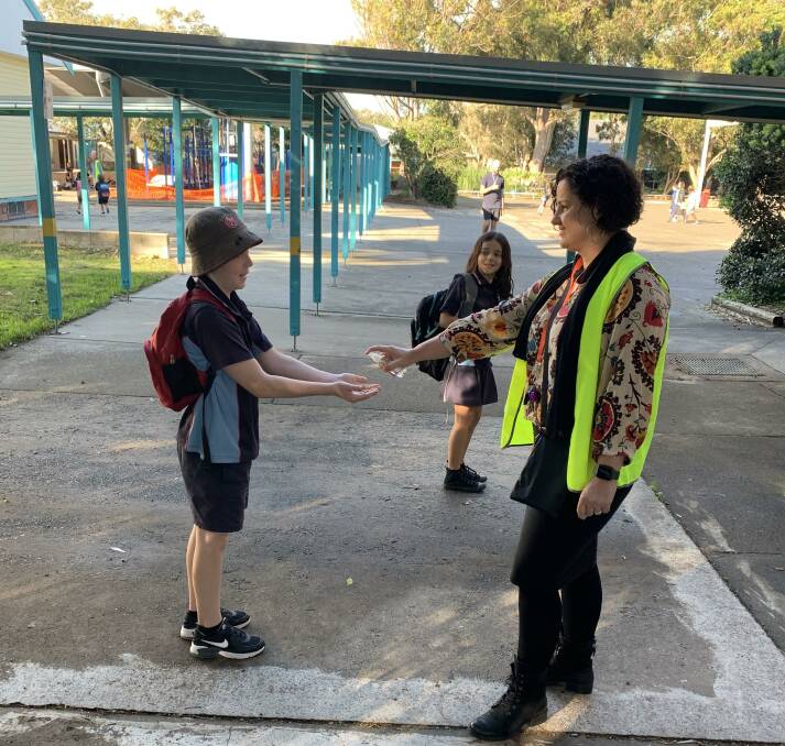 Deputy principal, Tianne Buderus, greets Angus and his sister Ebony with hand sanitiser at Forster Public School.