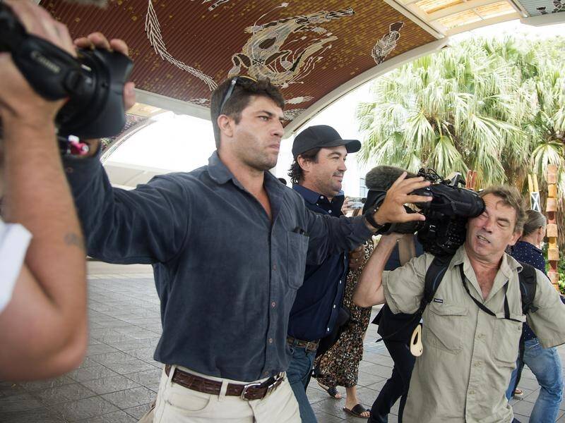 Minders jostle the media as Outback Wrangler star Matt Wright, centre, arrives at Darwin airport. (Aaron Bunch/AAP PHOTOS)