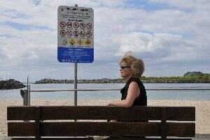 WARNING SIGN INEFFECTIVE: Eileen Marks sits beside the generic council sign with an easily-overlooked icon of the dangerous current swimmers must be wary of at Tuncurry Rockpool.   